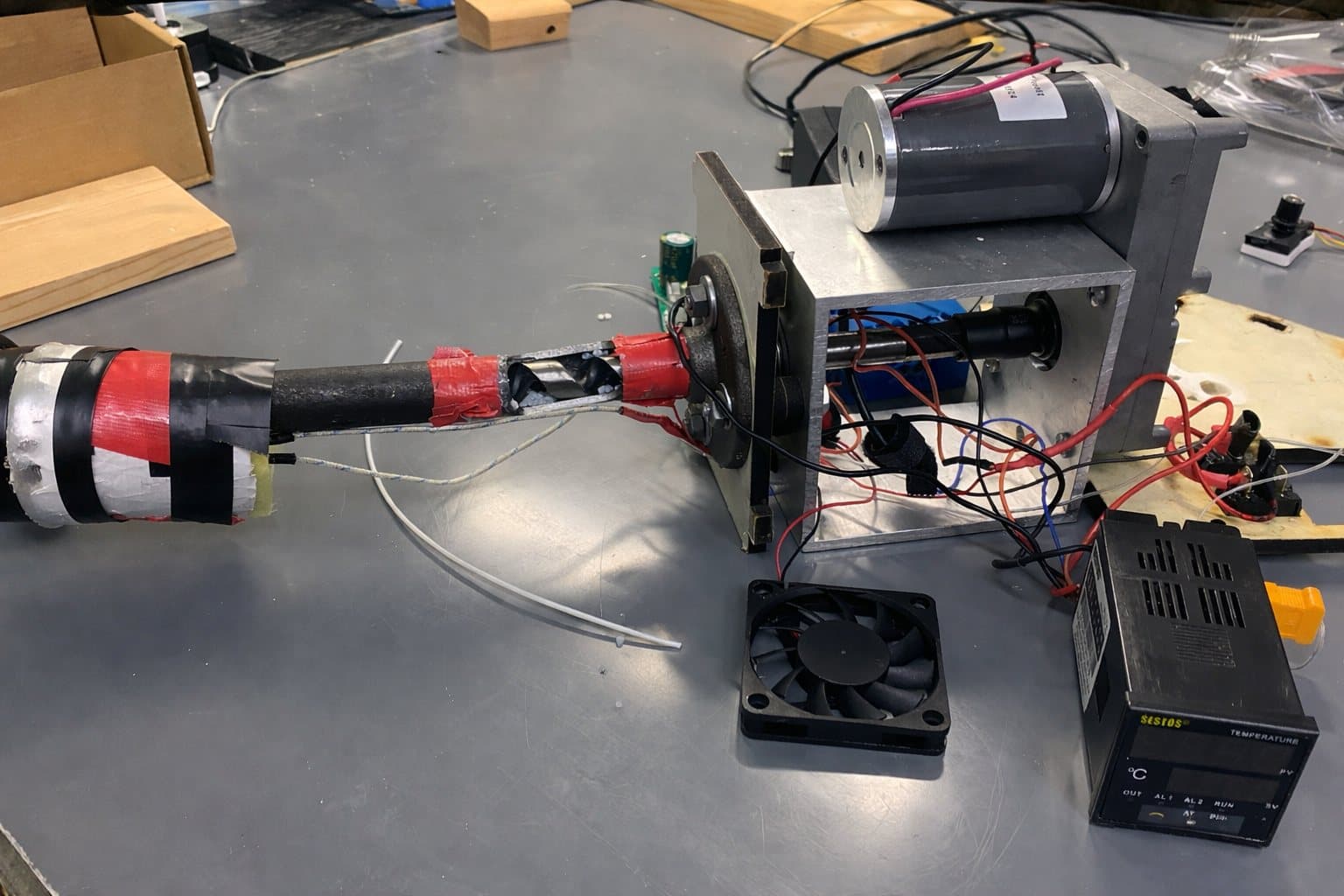 The inherited FilaStruder on the bench: horizontal barrel wrapped in tape, exposed wiring, ad-hoc temperature controller